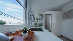 Een moderne keuken met een groot raam, witte kasten en roestvrijstalen apparatuur.
