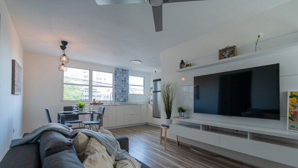 Een moderne woonkamer met een grote flatscreen-tv, een bank, een eethoek en een keuken op de achtergrond.