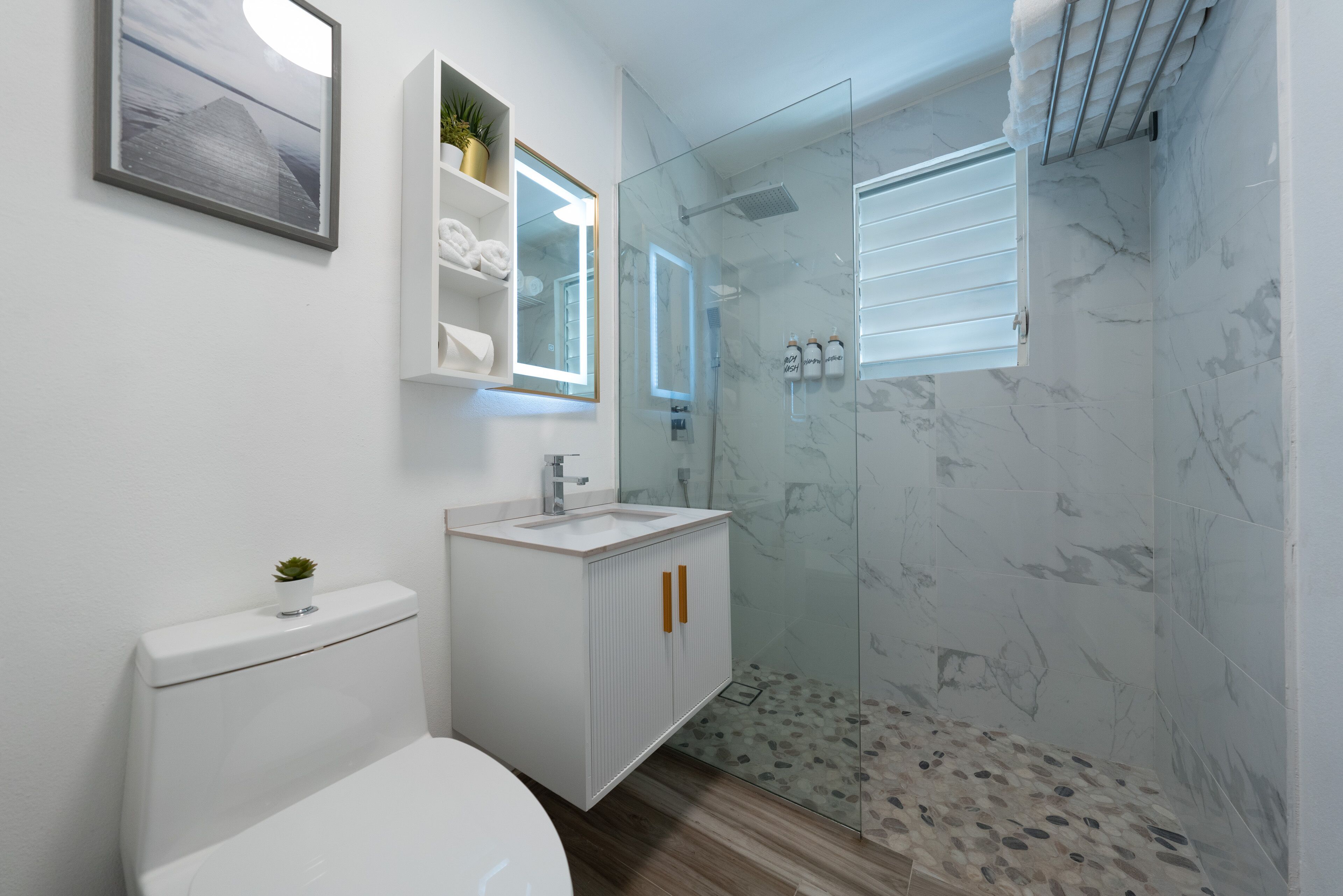 Een moderne badkamer met een glazen douchecabine, een witte wastafel en een toilet.