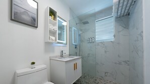 Een moderne badkamer met een glazen douchecabine, een witte wastafel en een toilet.