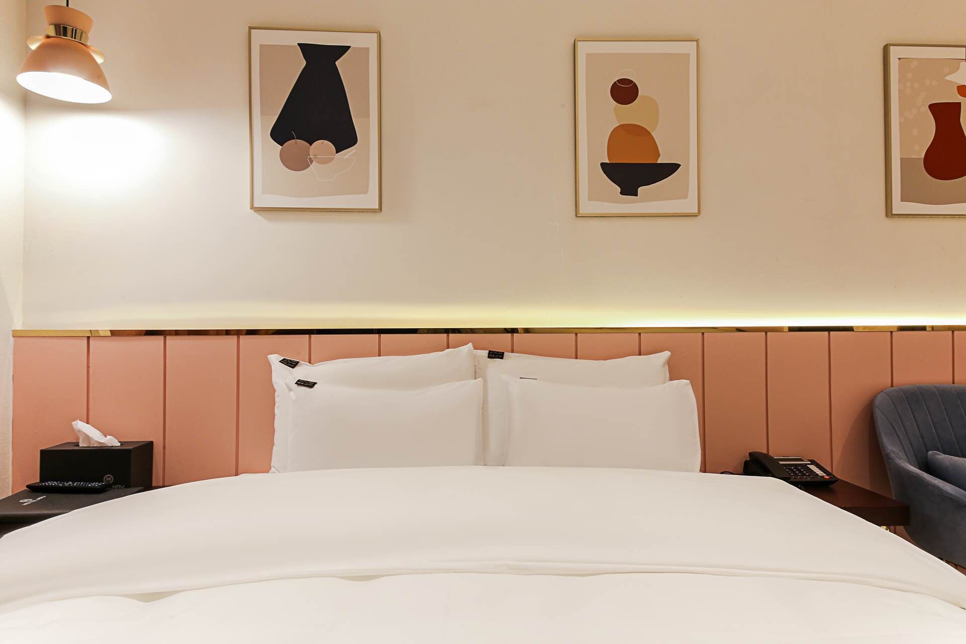 A hotel room with a bed, a bedside table with a lamp, a chair, and artwork on the wall.