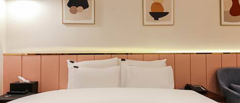 A hotel room with a bed, a bedside table with a lamp, a chair, and artwork on the wall.