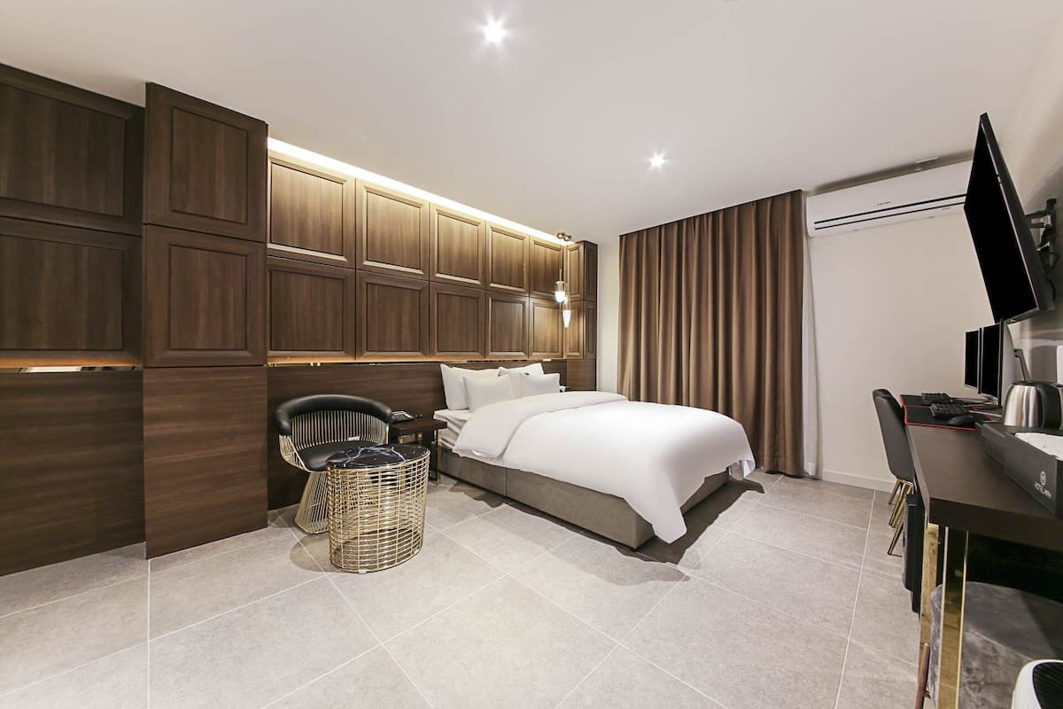 A modern hotel room with a large bed, a desk with a computer, a TV, and a seating area with a chair and a small table.