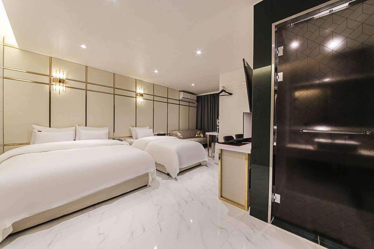 A modern hotel room with two beds, a desk, and a dark door.