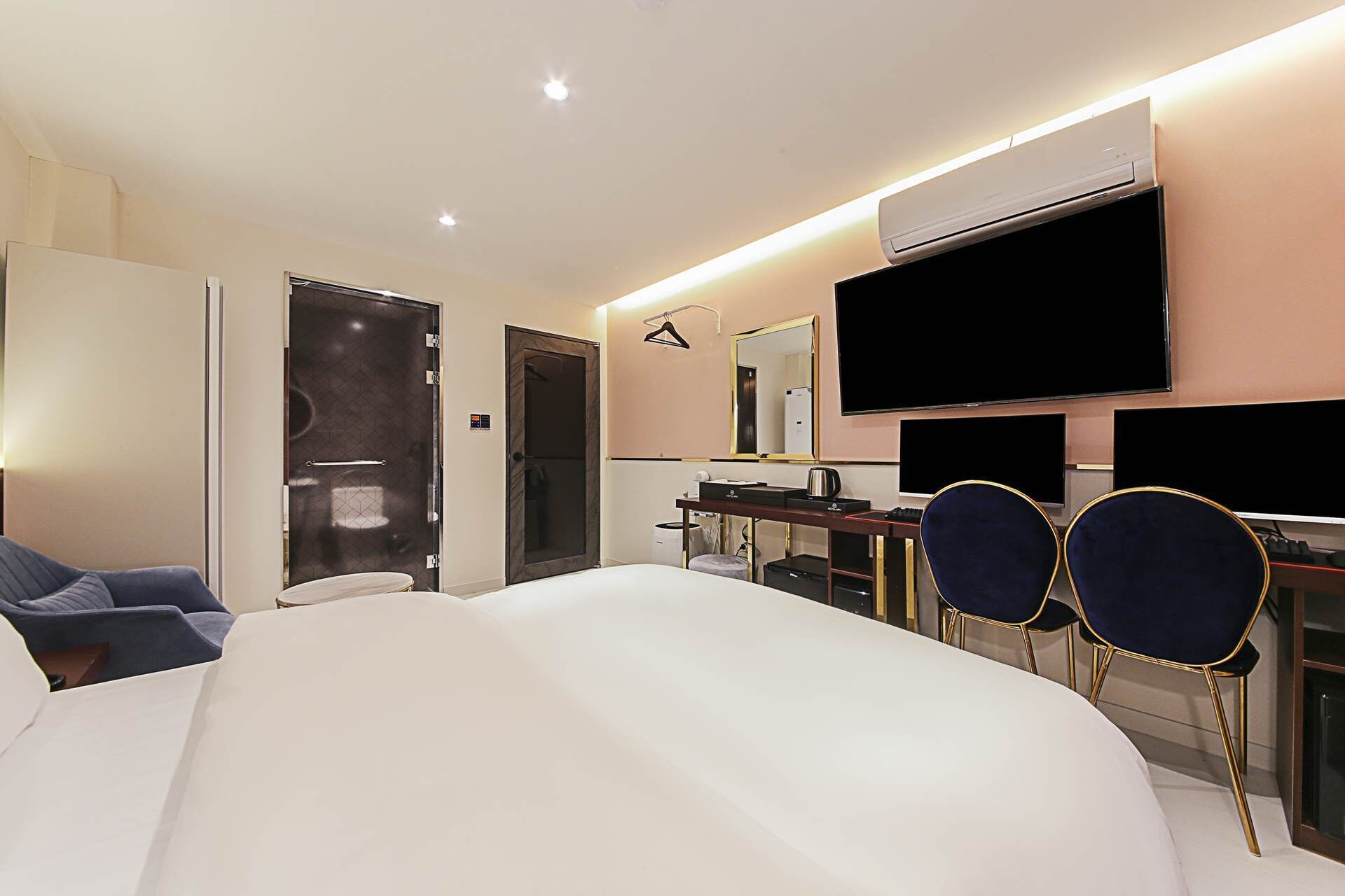 Habitación de hotel con una cama grande, un escritorio con computadora, dos sillas, un televisor y un aire acondicionado.