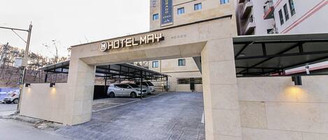 A hotel entrance with a covered parking area and a building with multiple floors and balconies.