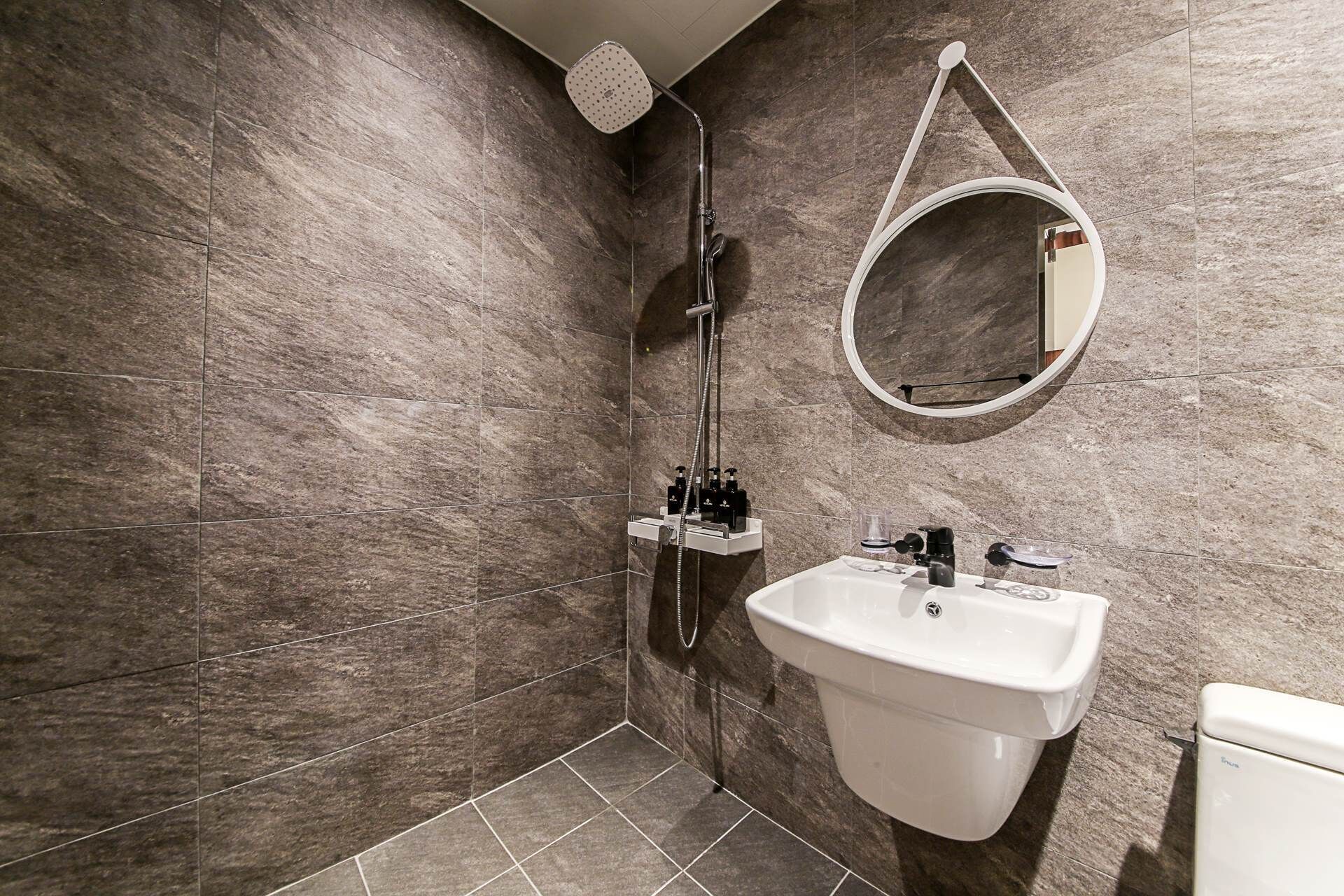 A modern bathroom with a shower, a sink, and a round mirror.