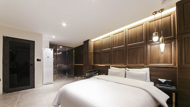 Una camera d'albergo moderna con un letto grande, pannelli di legno alle pareti, una scrivania integrata e un angolo doccia.
