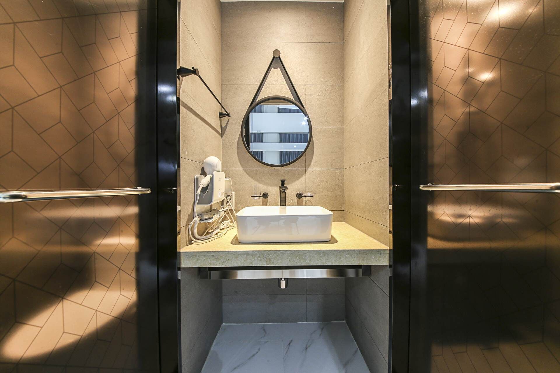 A modern bathroom with a rectangular sink, a round mirror, and a hairdryer on the counter.