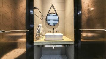 A modern bathroom with a rectangular sink, a round mirror, and a hairdryer on the counter.