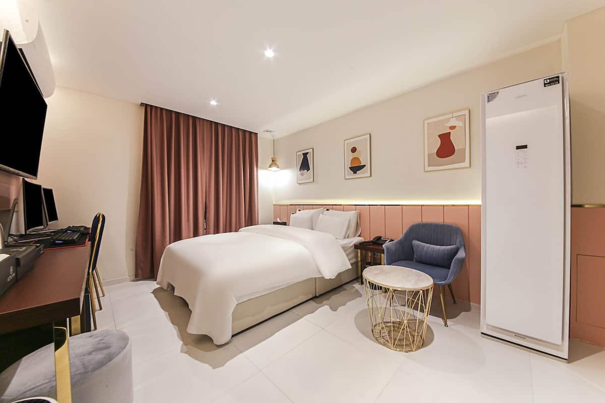A hotel room with a bed, a desk with a computer, a chair, a round table, and a refrigerator.