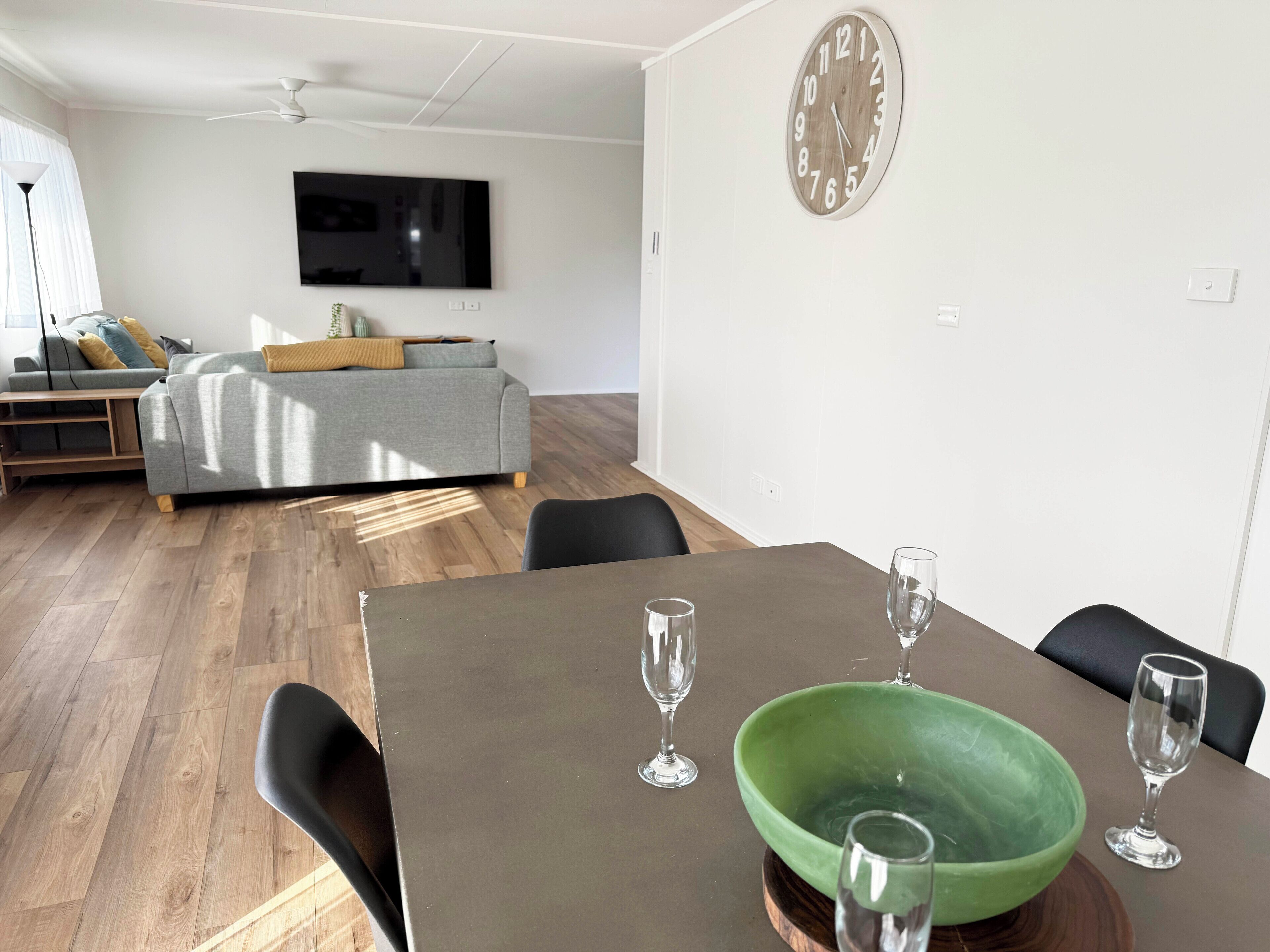 Uma sala de estar moderna com um sofá cinzento, uma televisão de tela plana e um espaço de refeições com uma mesa e cadeiras de madeira.