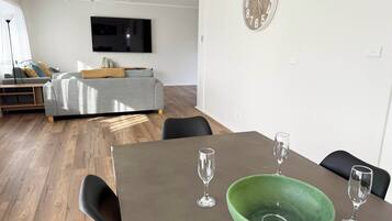 Uma sala de estar moderna com um sofá cinzento, uma televisão de tela plana e um espaço de refeições com uma mesa e cadeiras de madeira.