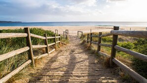 Un sentier en bois mène à une plage d’où l’on a une vue dégagée sur l’océan.