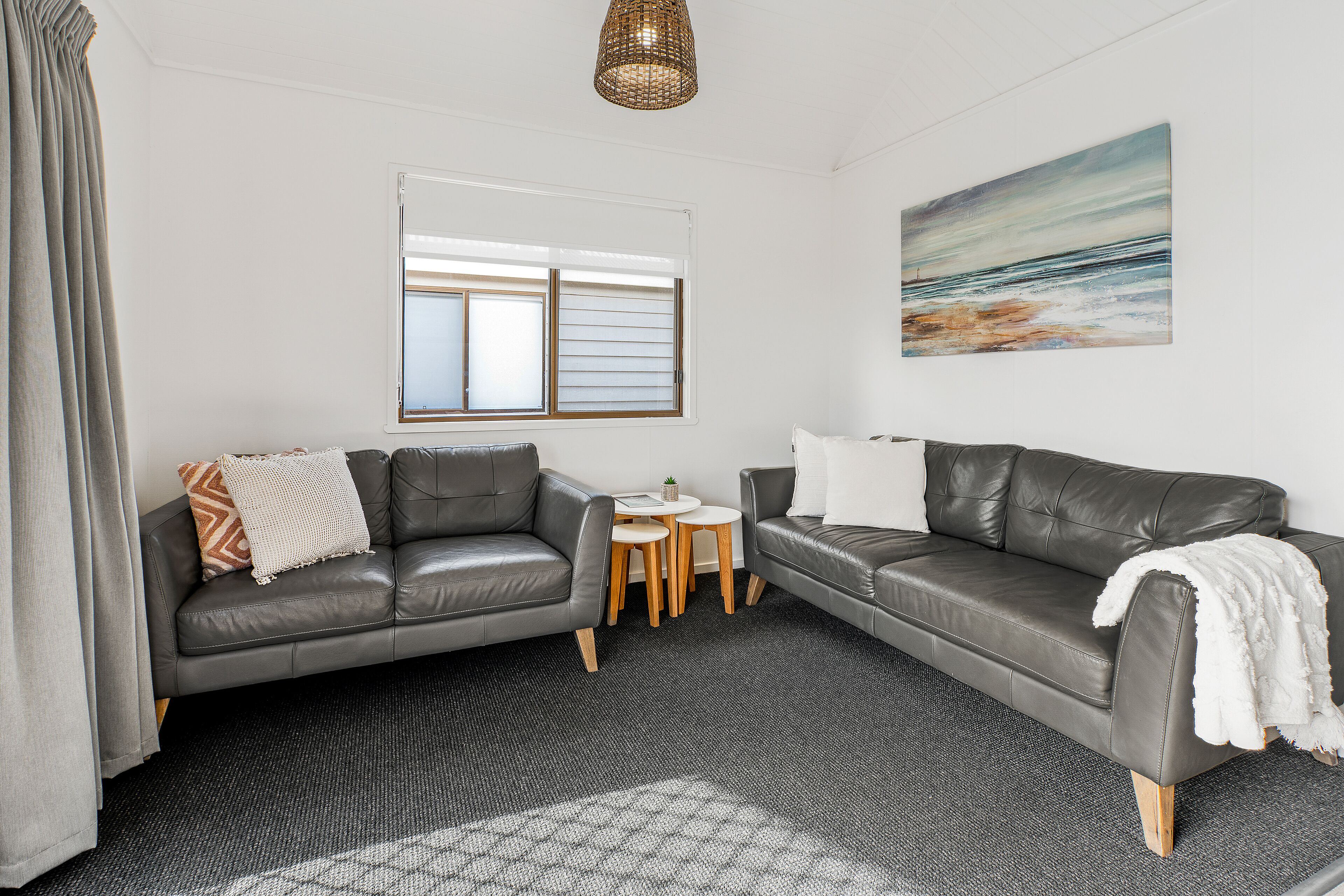 A modern living room with two leather sofas, a small round table, and a large window with blinds.