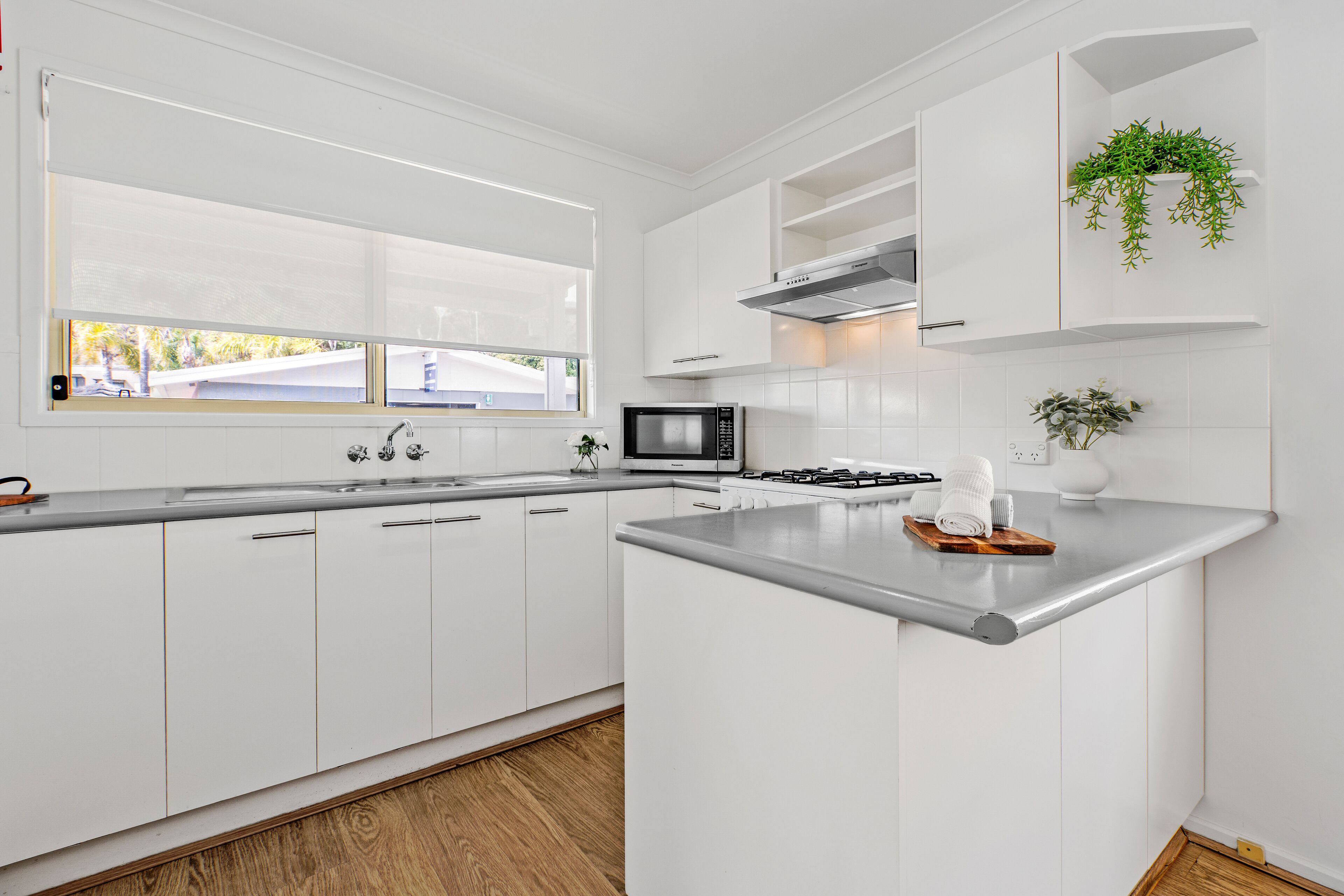 Une cuisine moderne avec des meubles blancs, un four à micro-ondes en acier inoxydable et une cuisinière intégrée.