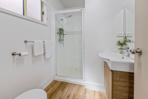Een moderne badkamer met een douchecabine van glas, een houten vloer, een wit toilet en een wastafel met spiegel.