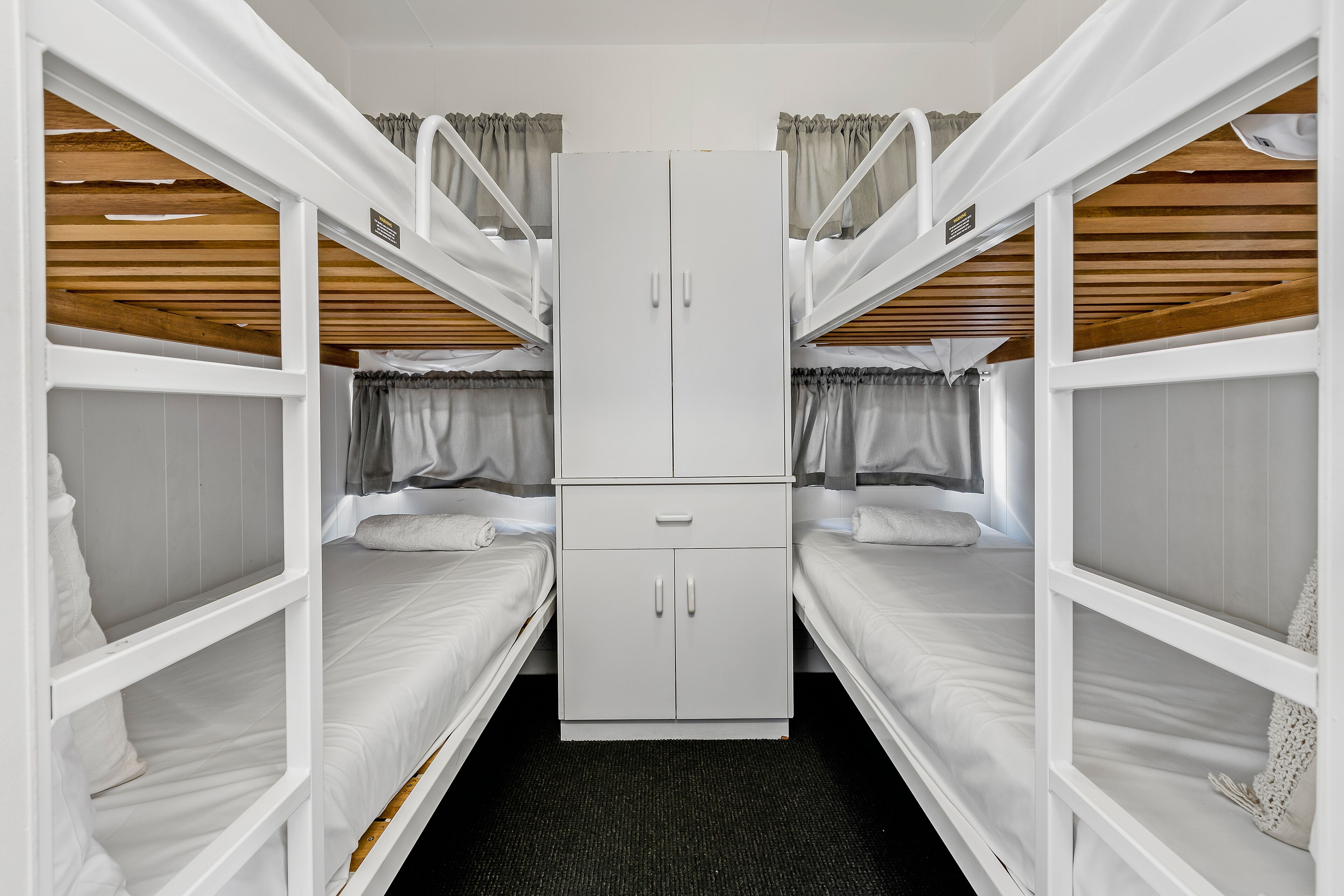 Un dormitorio con literas dobles, un armario blanco y un pequeño escritorio.