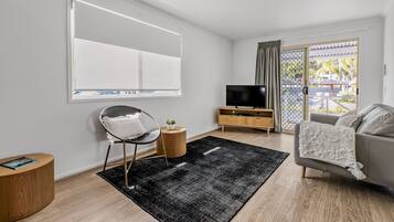 A modern living room with a flat-screen TV, a grey sofa, a round wooden side table, and a black rug.