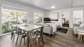 Un salon spacieux doté d’une grande fenêtre, un coin repas avec une table en verre et un espace détente confortable avec un canapé et un téléviseur.