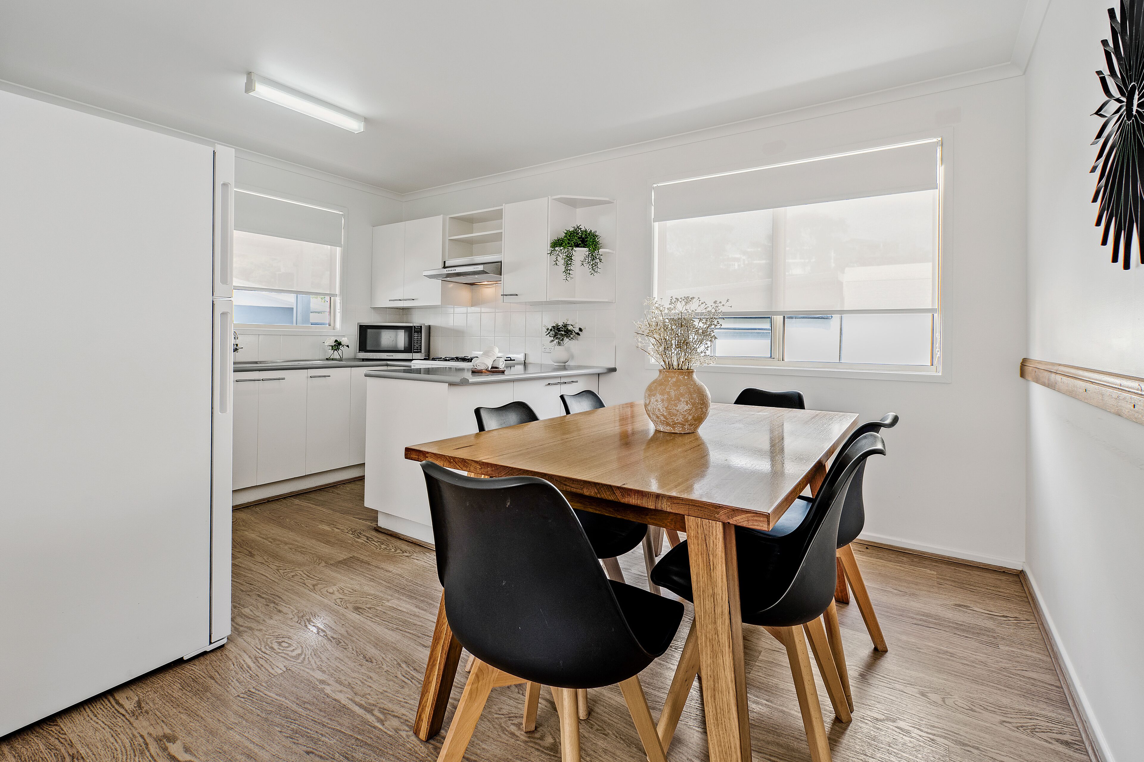 A modern kitchen with white cabinetry, a wooden dining table, and black chairs.
