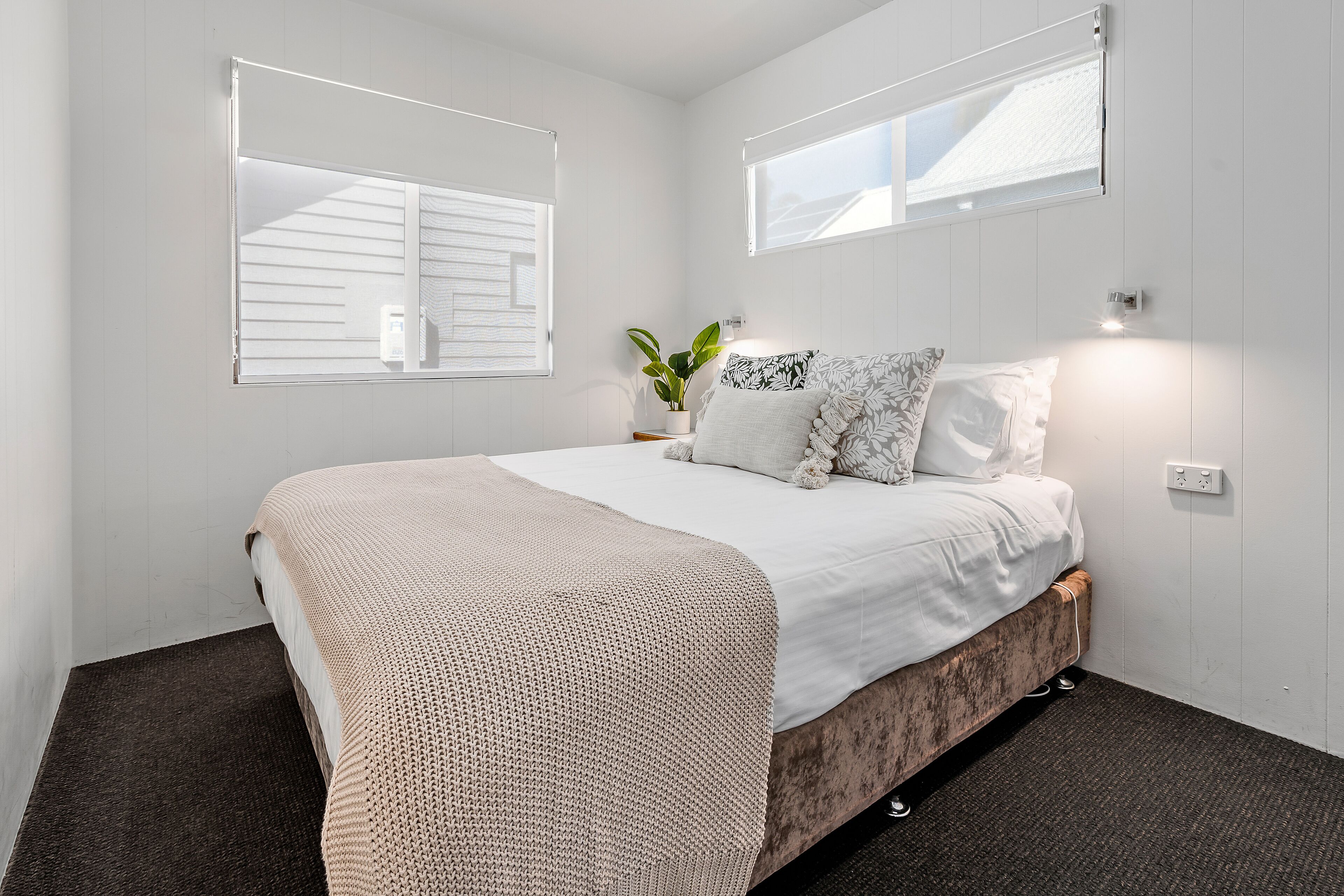 A bedroom with a bed, a potted plant, and a window.