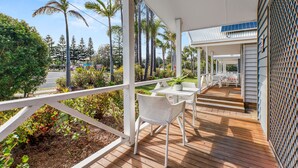 Une terrasse extérieure couverte, dotée de mobilier blanc, offrant une vue sur la rue et surmontée d’un panneau solaire sur le toit.