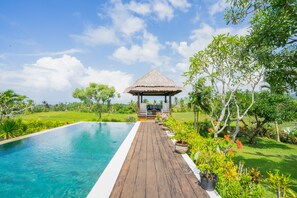 A wooden deck leading to a thatched-roof gazebo by a clear blue pool. - Villa Labak Sari Tabanan (Selemadeg)