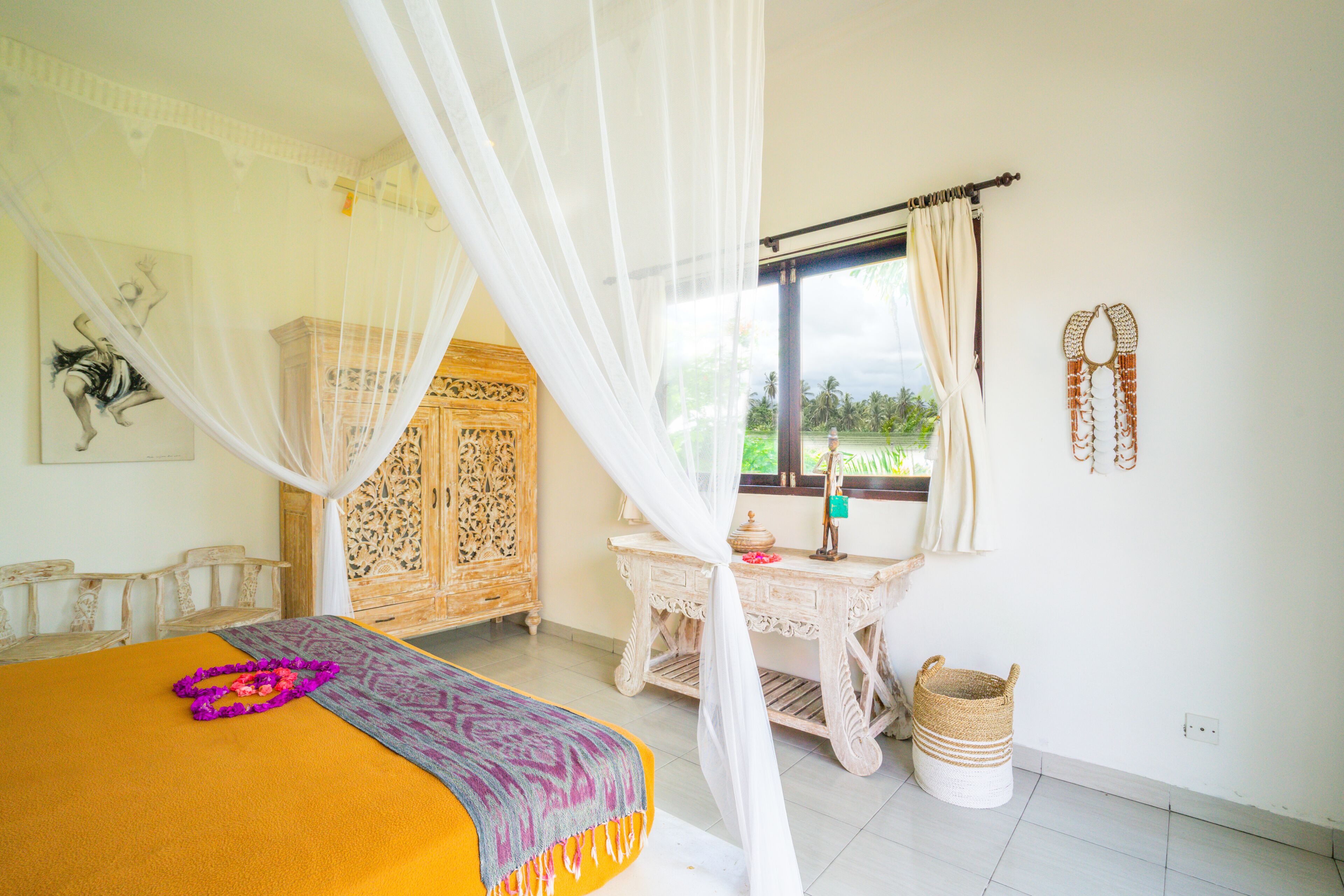 A bedroom with a bed, a nightstand, a window with curtains, a wooden wardrobe, and a wall-mounted decorative item.