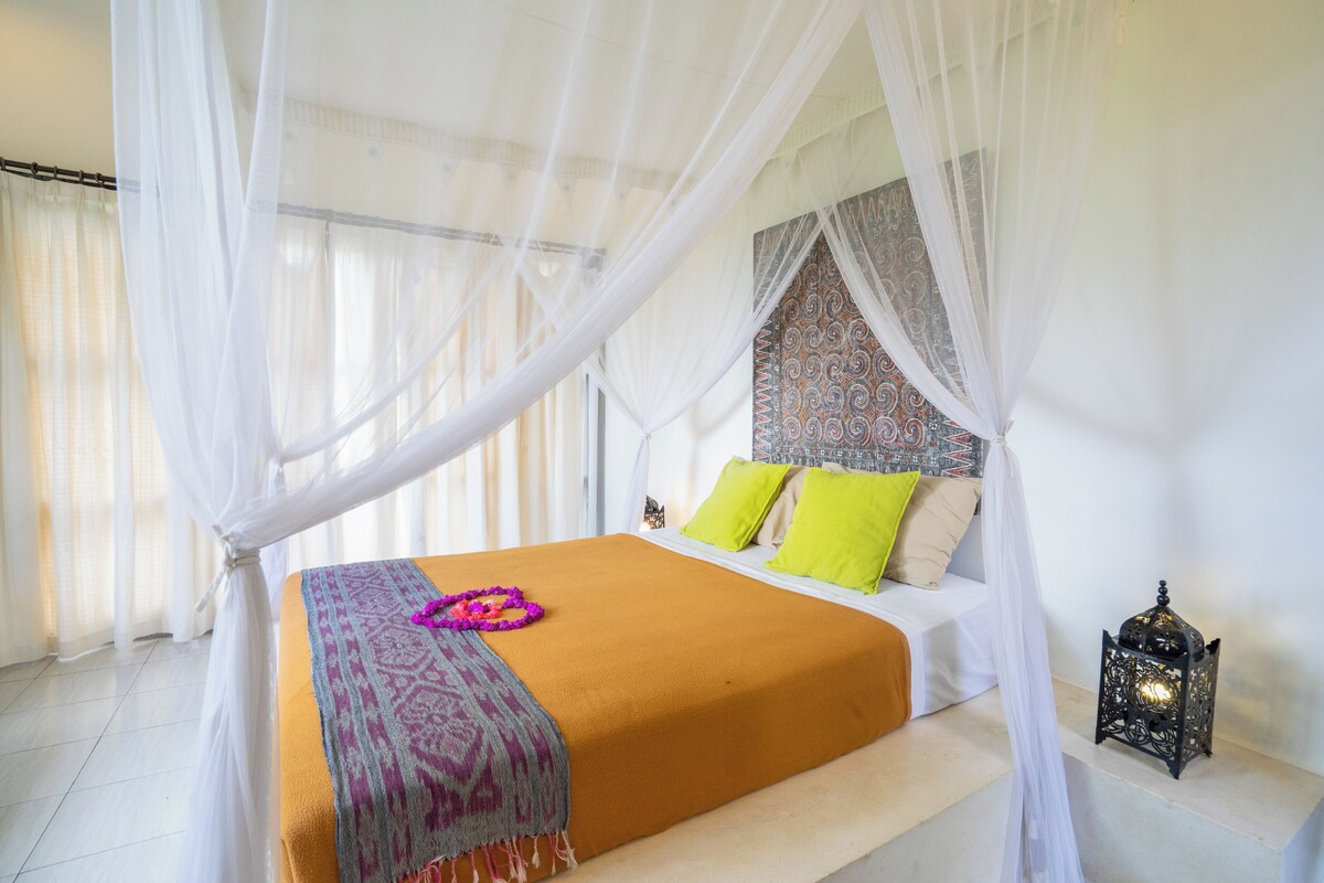A bed with a white canopy, a patterned throw, and green pillows.