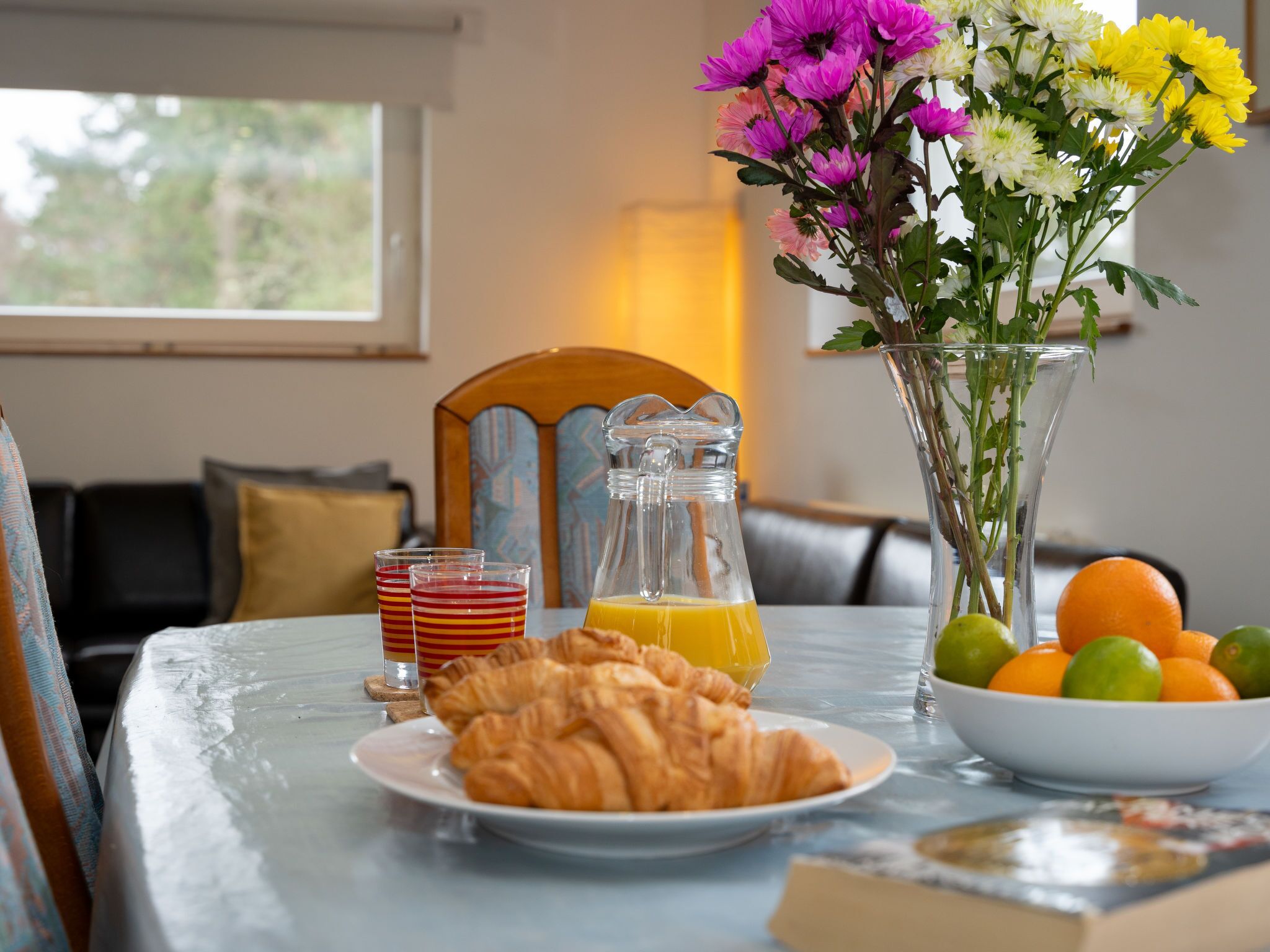A breakfast table with croissants, orange juice, and a vase of flowers.