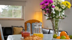 A breakfast table with croissants, orange juice, and a vase of flowers. - Muir Edge by Interhome (Nethy Bridge)