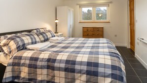 A bedroom with a bed, a nightstand, a dresser, a window, and a door. - Muir Edge by Interhome (Nethy Bridge)