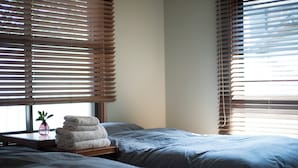 A bedroom with two beds, a bedside table with a plant, and a window with blinds. - AMIGO HOUSE - Hostel (Zushi)