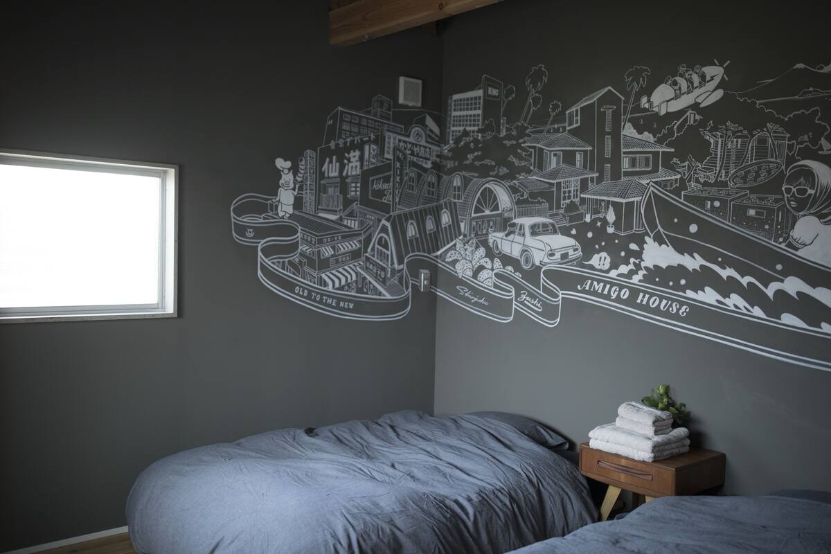 A bedroom with a bed, a small wooden nightstand, and a wall mural depicting a city scene.