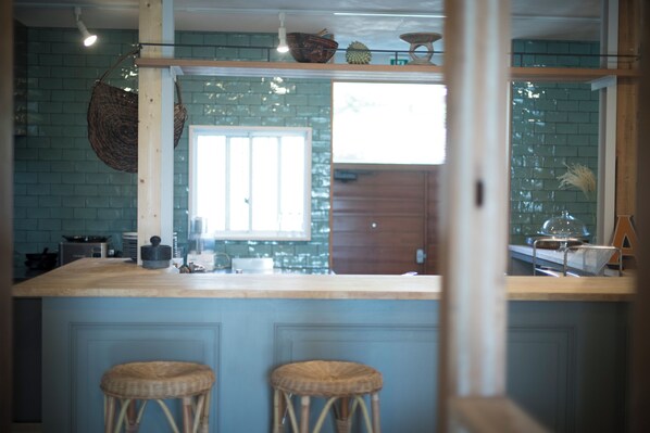 A kitchen with a wooden countertop, two wicker stools, and a window with blinds.