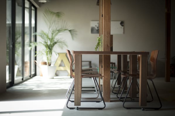 Un interior moderno con una mesa y sillas de madera, ventanas amplias y una planta en maceta.