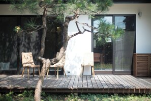 Una terraza de madera con tres sillas de mimbre y un árbol.