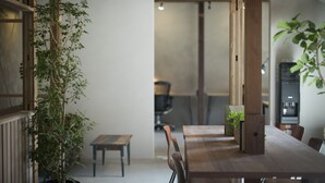 A modern dining area with a wooden table, chairs, and potted plants. - AMIGO HOUSE - Hostel (Zushi)