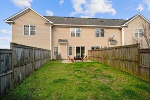 A two-story house with a fenced backyard, a patio with outdoor furniture, and a satellite dish.