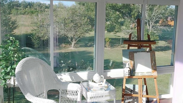 A room with a large window, a ceiling fan, a rocking chair, a small table with a teapot, and an easel with a blank canvas. - Sleeps up to 8 in a safe, quiet area (Kodak)