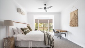 Una camera da letto con un letto, un comodino, una lampada e vista all'esterno attraverso un'ampia finestra.