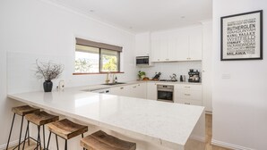 Una cucina moderna con mobili bianchi, una grande isola con sgabelli da bar, un forno a microonde e una macchina per il caffè.