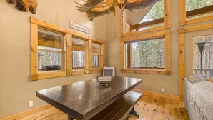 Una habitación con una mesa de madera, un banco y un cartel que dice 'HELLO THERE'. Hay ventanas con marcos de madera y un cartel sobre una ventana que dice 'Go Jump in the Lake'.