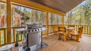 Una terraza cubierta al aire libre con una parrilla, muebles de madera y vistas a un bosque.