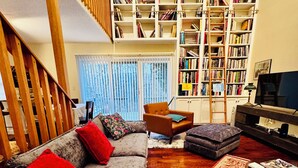 A living room with a grey sofa, red cushions, a wooden staircase, a bookshelf, and a television. - Perfect Family Gateway Spot for the Berkshires, Jiminy Peak Skiing, MASS MoCA (Hancock)