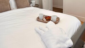 A neatly made bed with a tray of breakfast items including muffins and cups, and a rolled-up towel on the bed. - Boston Hospitality Homes, Harvard (Boston)