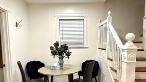 A dining area with a round table, four chairs, a vase with flowers, and a window with blinds. - Boston Hospitality Homes, Harvard (Boston)