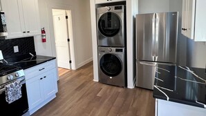A modern kitchen with stainless steel appliances, a double oven, and a built-in washer and dryer. - Boston Hospitality Homes, Harvard (Boston)