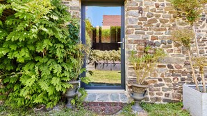 A stone building with a dark door, potted plants, and a clear view of a red-roofed building in the background. - Le Hamelinet by Interhome (Surville)